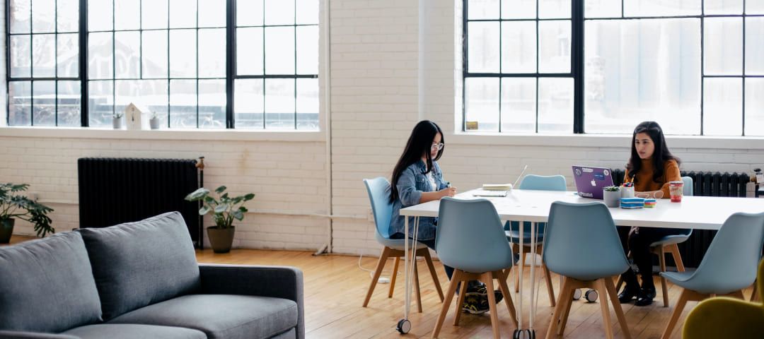 Photo of two women working at a table in a large office