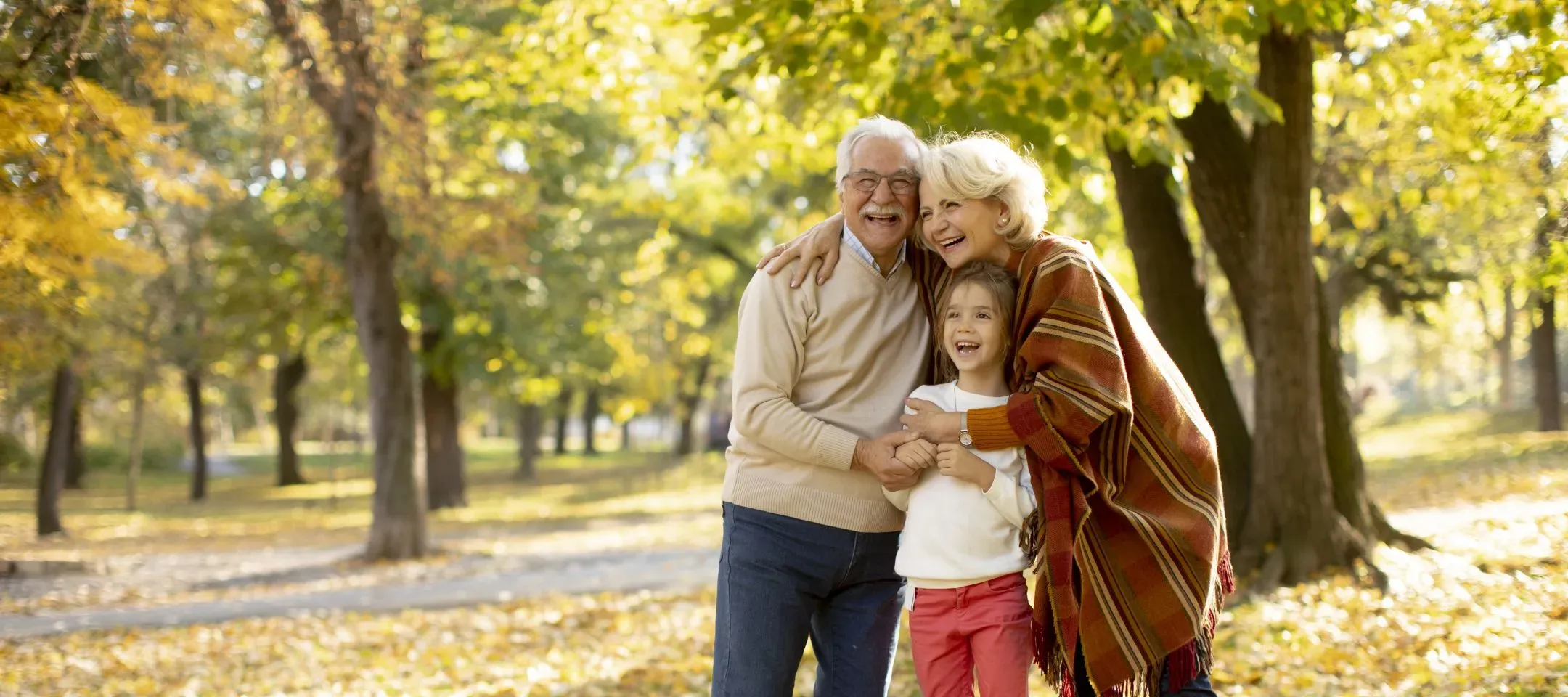 WTC Communications Kingston - Happy grandparents and their grandchild laughing and embracing in an autumn park, enjoying family time.