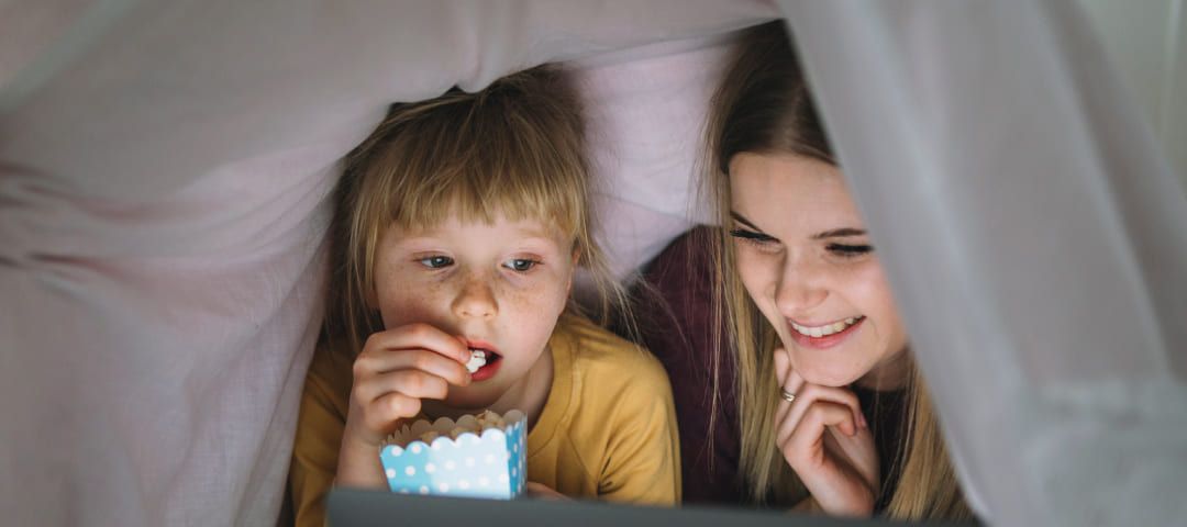 Photo of a woman and a child looking at a computer under pillows