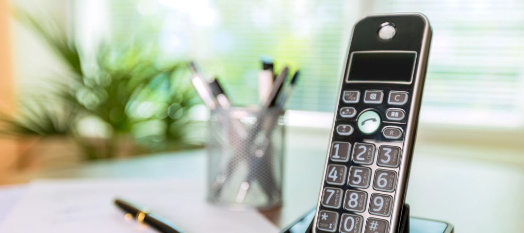 Telephone on wooden desk next to paper and pen