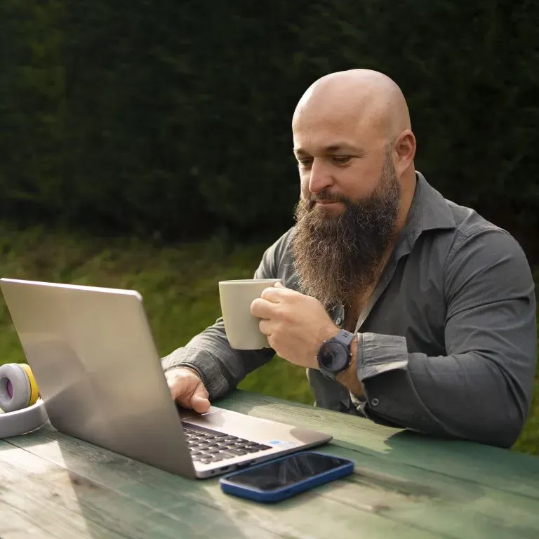 WTC Communications Perth - Bearded man working on a laptop and drinking coffee outdoors, enjoying reliable internet.