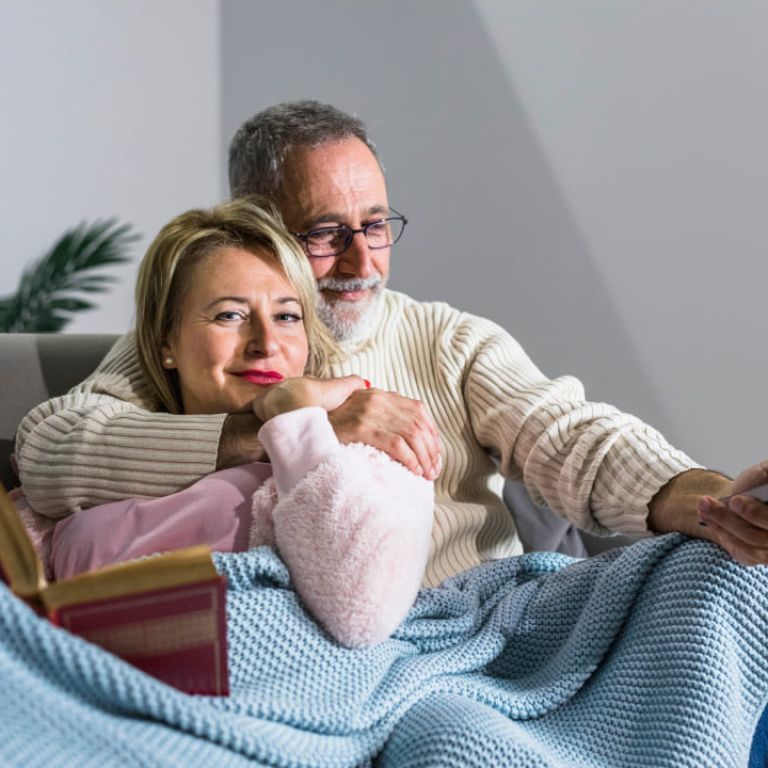 Photo of a man and a woman sitting on a couch; the man is pointing a remote control